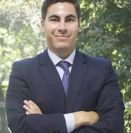 Hombre sonriente con traje y corbata delante de árboles.