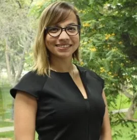 Mujer con gafas y vestido negro, sonríe al aire libre.