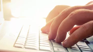 Manos escribiendo en un teclado de computadora blanca iluminada.