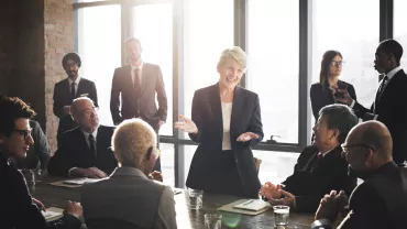 Una mujer lidera una reunión de negocios en una sala con luz natural.