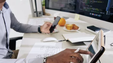 Hombre trabajando en escritorio con computadora y tablet.