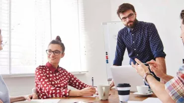 Grupo de personas en reunión alrededor de una mesa con portátil y café.