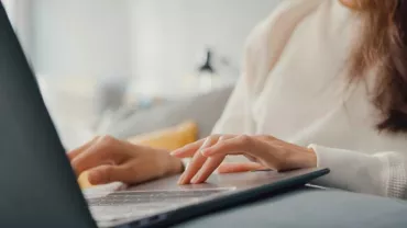 Mujer en suéter blanco usando computadora portátil en sofá.