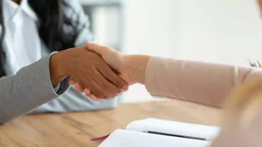 Dos personas dándose la mano sobre una mesa de madera.