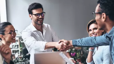 Grupo de personas en una reunión de oficina, dos hombres estrechando manos.