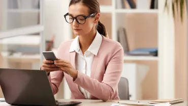 Mujer en oficina usando teléfono y portátil.