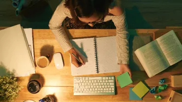 Persona trabajando en un escritorio con libreta abierta y varios papeles de colores.
