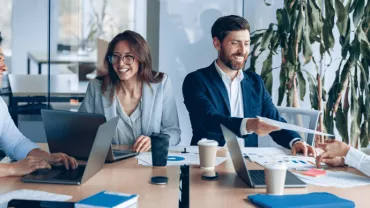 Grupo de personas en reunión de trabajo con portátiles en la mesa.