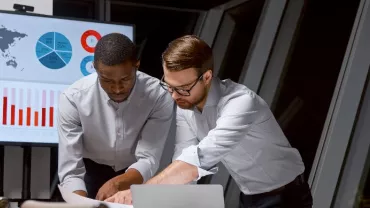 Dos hombres revisando documentos con gráficos en una oficina.