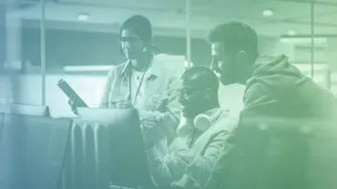Tres personas trabajando juntas en una oficina con computadoras.
