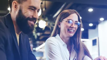 Dos personas sonrientes mirando una pantalla en una oficina moderna.
