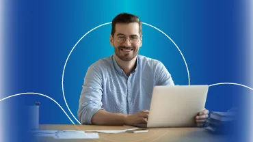 Hombre sonriente con gafas usando una laptop, fondo azul.