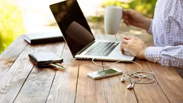Persona trabajando al aire libre con laptop y taza de café.