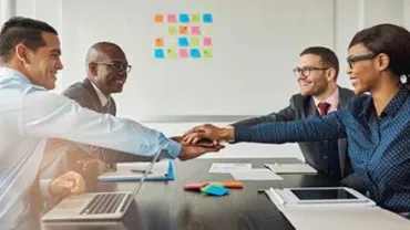Grupo de personas sonrientes en una reunión de negocios, uniendo manos sobre la mesa.