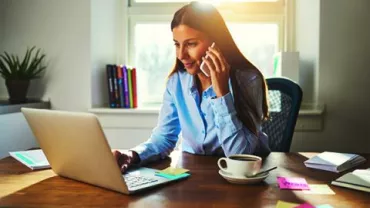 Mujer trabajando en una laptop y hablando por teléfono.