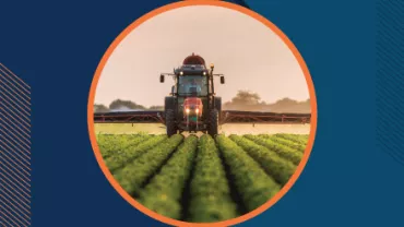 Tractor fumigando un campo al atardecer.