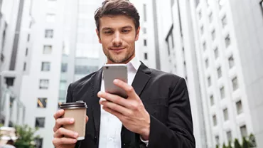 Hombre en traje sonríe mientras mira su teléfono en la calle.