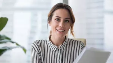 Mujer sonriendo con camisa de rayas, sosteniendo papeles.