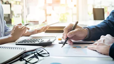 Personas trabajando en documentos y gráficos con calculadora y tablet.