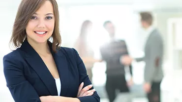 Mujer sonriente en primer plano con colegas difuminados al fondo.
