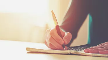 Persona escribiendo en un cuaderno con buena iluminación.