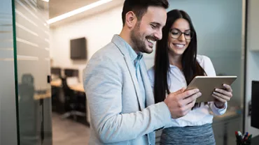 Pareja de profesionales sonriendo mientras revisan una tableta en la oficina.