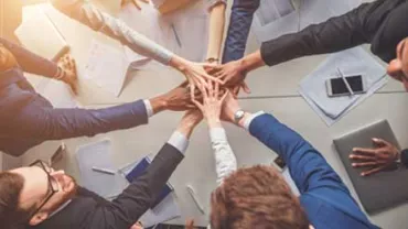 Personas uniendo manos en un gesto de trabajo en equipo.