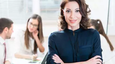Mujer sonriendo con equipo trabajando detrás.