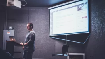 Hombre presentando en una pantalla grande con proyector.