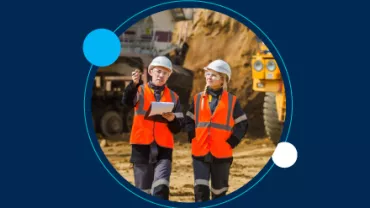 Dos ingenieros con chalecos naranjas discuten en un sitio de construcción.