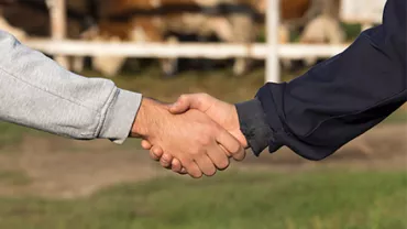 Dos personas estrechándose la mano en un entorno rural.