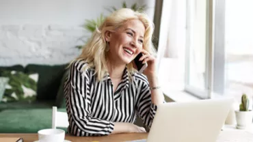 Mujer sonriendo hablando por teléfono junto a computadora.