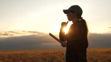 Persona en un campo con una tableta al atardecer.