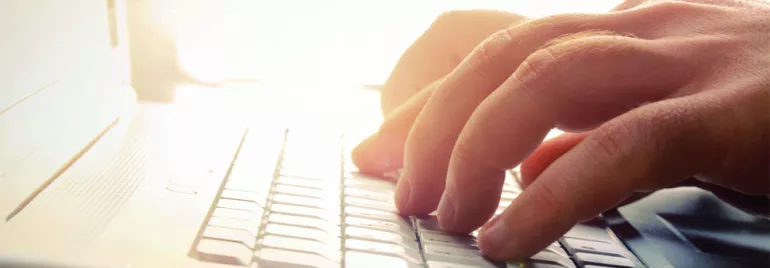 Manos escribiendo en un teclado de computadora blanca iluminada.