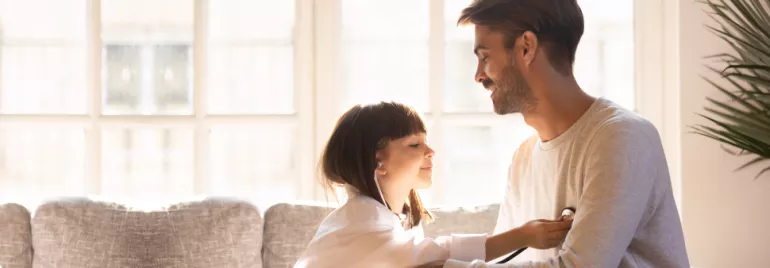 Niña jugando a ser doctora revisa a su padre con un estetoscopio en casa.
