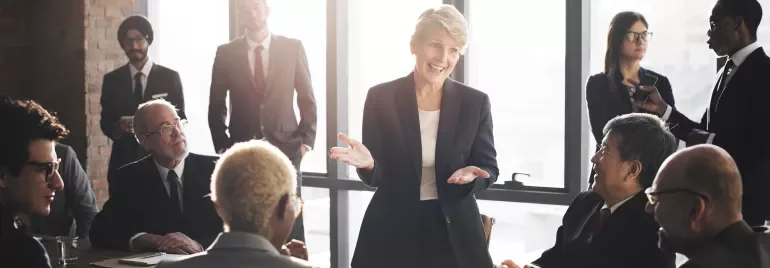 Una mujer lidera una reunión de negocios en una sala con luz natural.