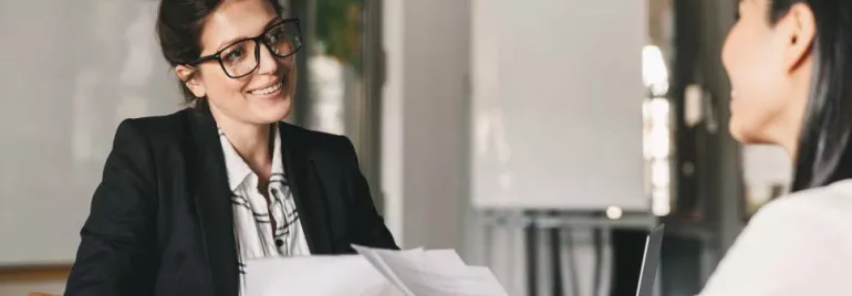 Mujer con gafas sonriendo mientras sostiene documentos en una reunión.