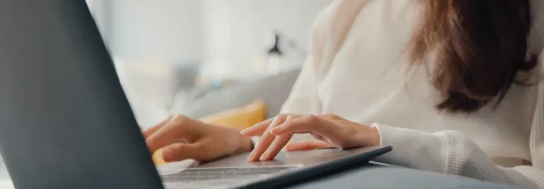 Mujer en suéter blanco usando computadora portátil en sofá.