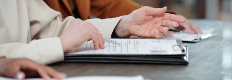 Manos revisando documentos en una mesa de madera.