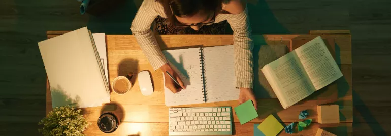 Persona trabajando en un escritorio con libreta abierta y varios papeles de colores.