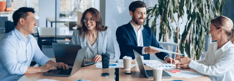 Grupo de personas en reunión de trabajo con portátiles en la mesa.