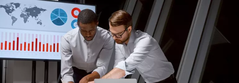 Dos hombres revisando documentos con gráficos en una oficina.