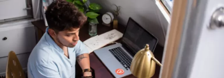 Persona escribiendo en una mesa con portátil y planta.