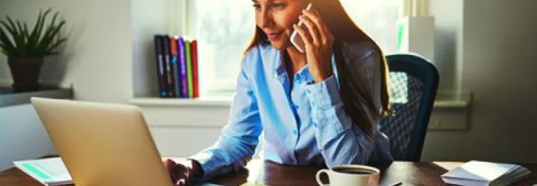 Mujer trabajando en una laptop y hablando por teléfono.
