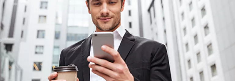 Hombre en traje sonríe mientras mira su teléfono en la calle.