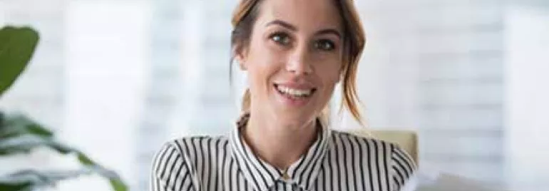 Mujer sonriendo con camisa de rayas, sosteniendo papeles.