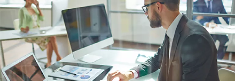Hombre con gafas trabajando en una oficina moderna con computadora y gráficos.
