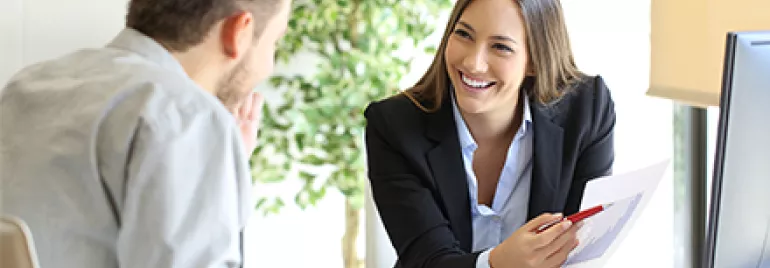 Dos personas conversando en una oficina, una mujer muestra un documento.
