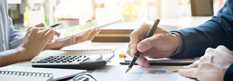 Personas trabajando en documentos y gráficos con calculadora y tablet.