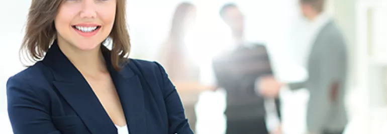Mujer sonriente en primer plano con colegas difuminados al fondo.
